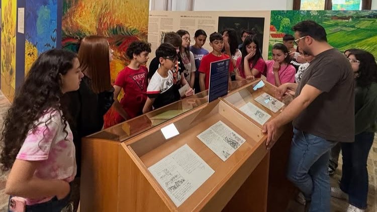 Un gruppo di studenti ascolta una guida davanti a una teca espositiva con lettere e opere di Van Gogh.