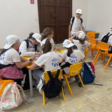 Una classe di bambini con cappellini bianchi impegnati in un laboratorio creativo con disegni e colori.