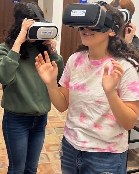 Due ragazze utilizzano visori di realtà virtuale con la scritta “Van Gogh”, sorridendo e interagendo con i contenuti immersivi.